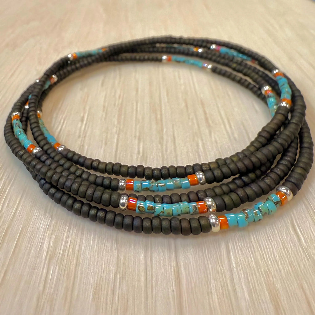 Handmade glass seed bead necklace with black, turquoise, orange, and silver beads on wood
