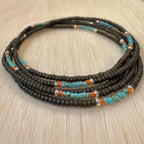 Handmade glass seed bead necklace with black, turquoise, orange, and silver beads on wood