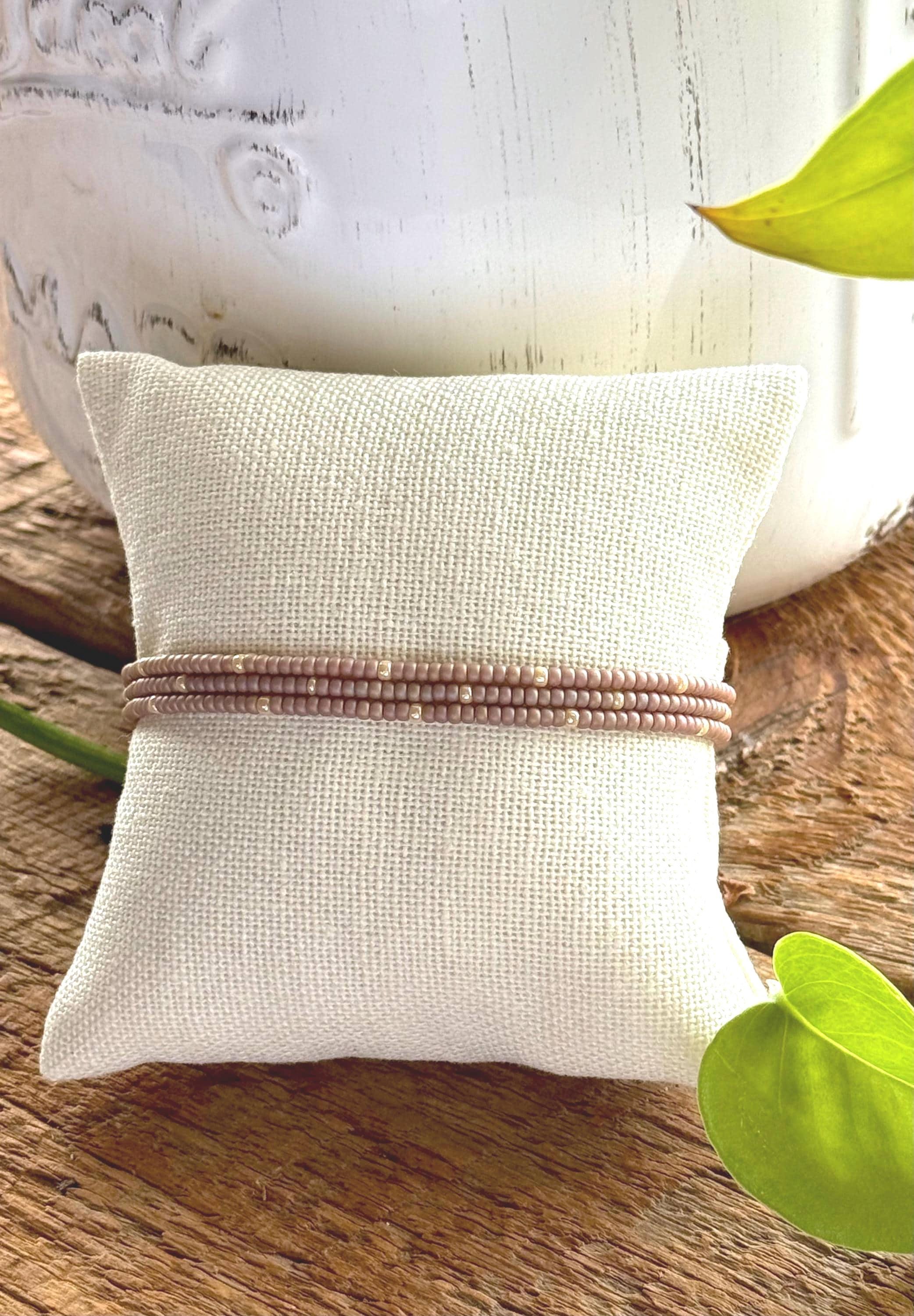 Handmade glass seed bead bracelet with muted pink beads, displayed on a linen cushion