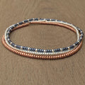 Handmade glass seed bead bracelet with gold, copper, and black beads on wood surface