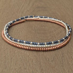 Handmade glass seed bead bracelet with gold, copper, and black beads on wood surface