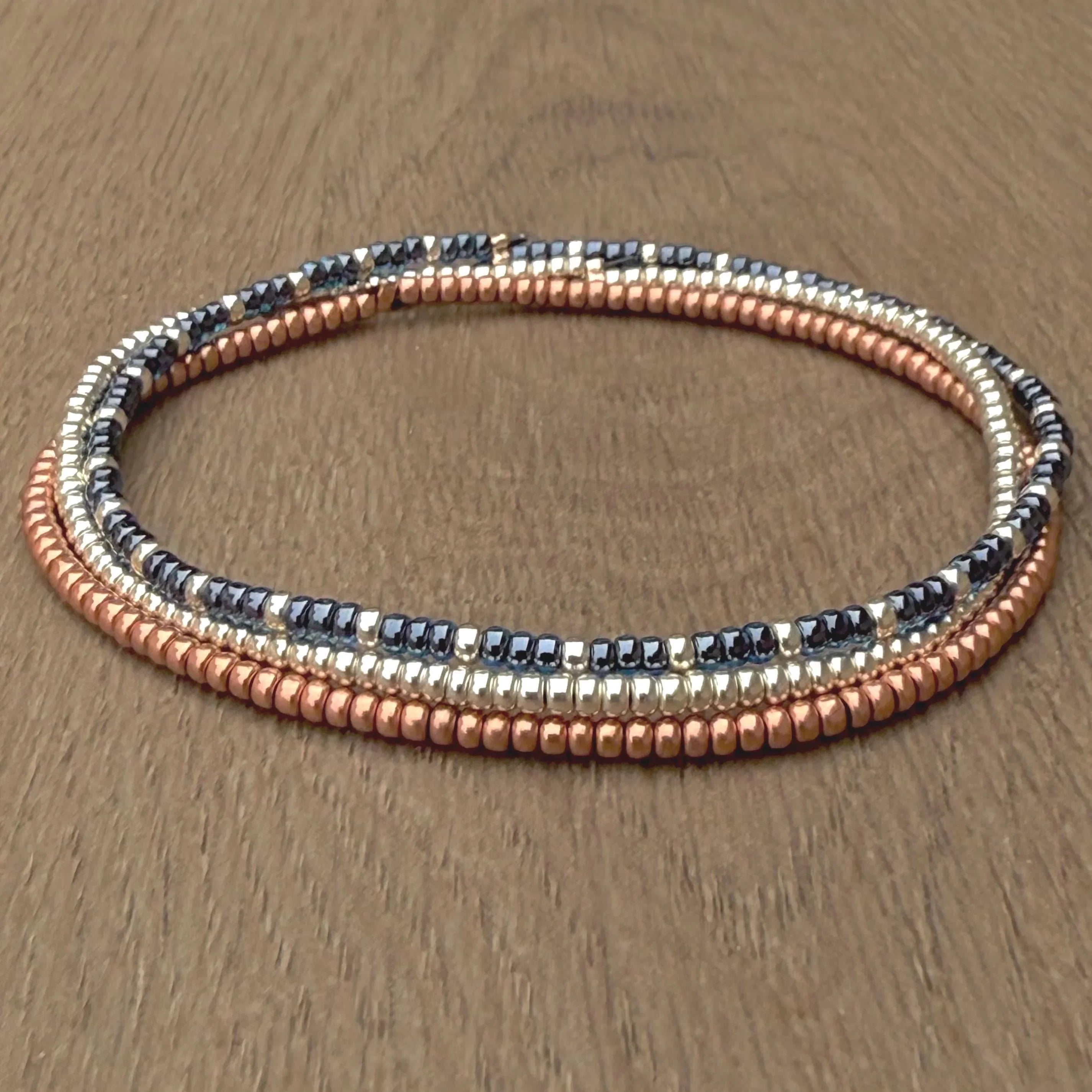 Handmade glass seed bead bracelet with gold, copper, and black beads on wood surface